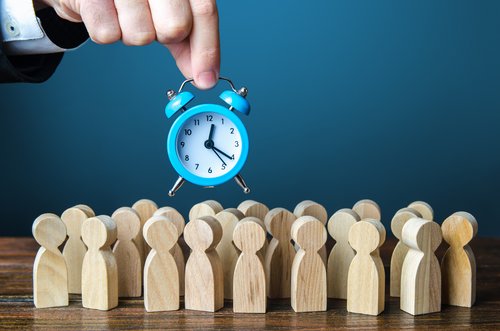 Ein Geschäftsmann hält einen Wecker über eine Menschenmenge. Zeitmanagement. Stundenlöhne, strenge Arbeitszeitgrenzen und Ruhezeit