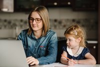 Mutter mit Kind sitzt vor Laptop und arbeitet
