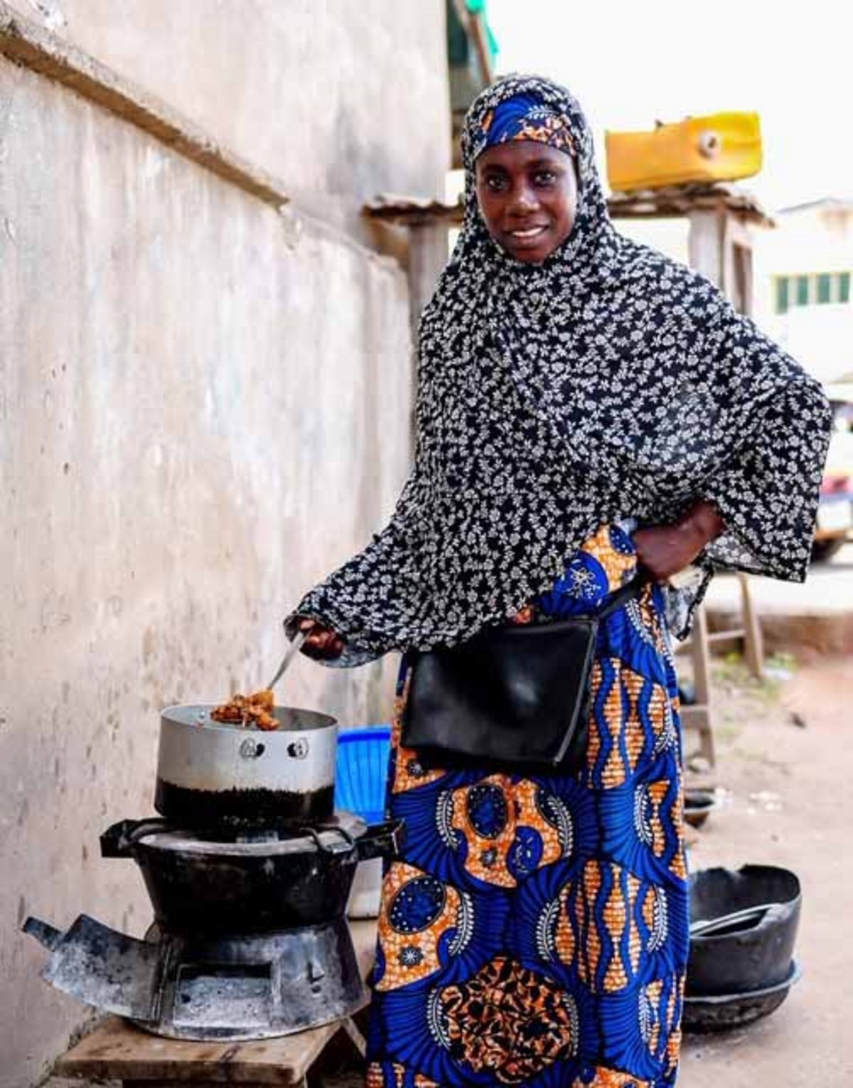 Eine Frau mit einem bunt gemusterten Kopftuch und einem bunt gemusterten Kleid rührt in einem Kochofen.