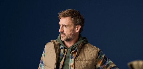 bärtiger Mann mit Karojacke, Hoody und beiger Weste