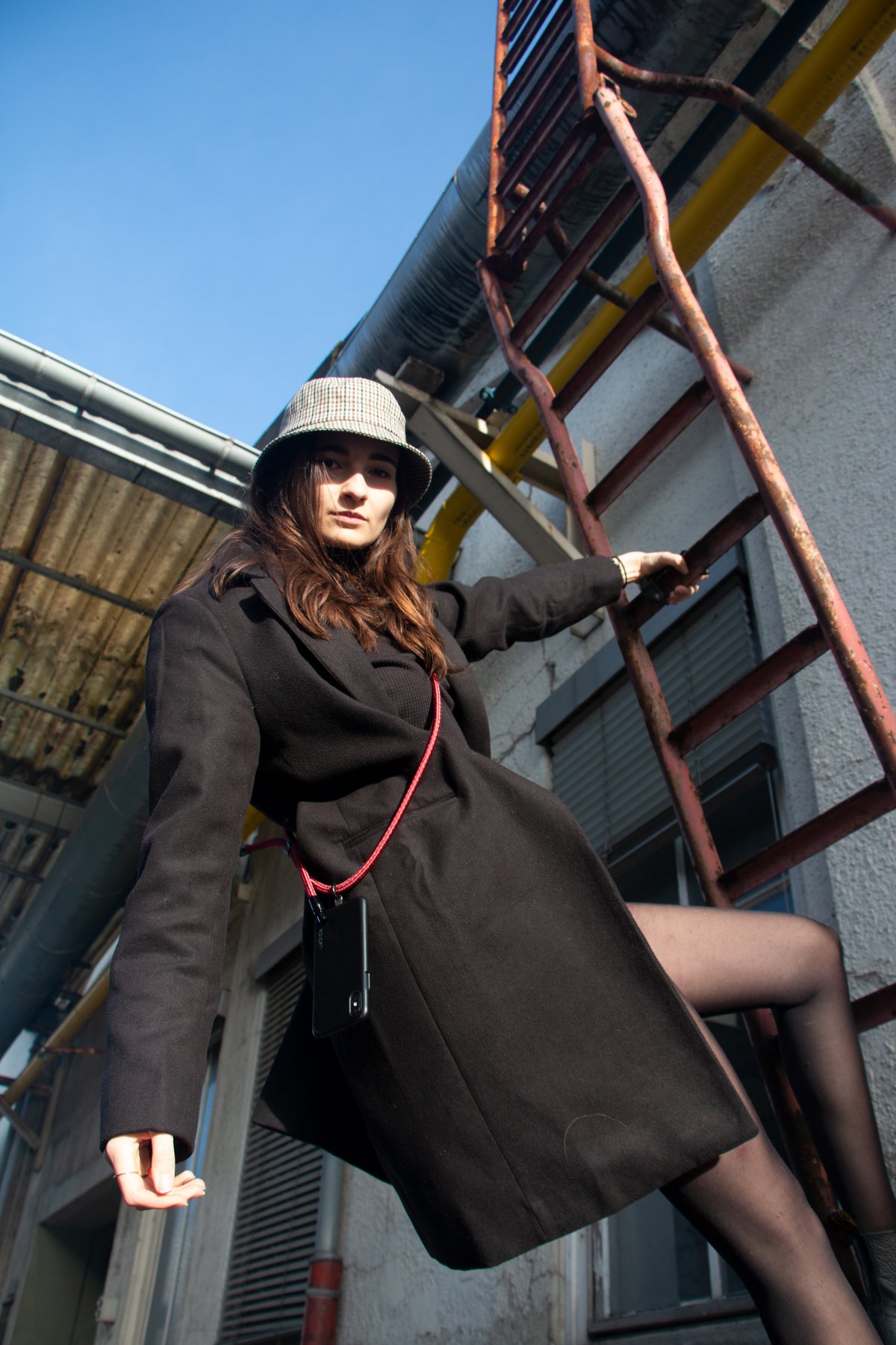Junge Frau steht auf Leiter und posiert lässig mit der Handykette von PortHy. 