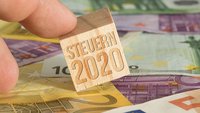 Hand hält Holzwürfel mit Schrift Steuer 2020 auf Eurogeldscheinen