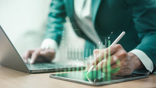 Person arbeitet an Laptop und Ipad mit grünem Diagramm, das grüne Berichterstattung darstellt.