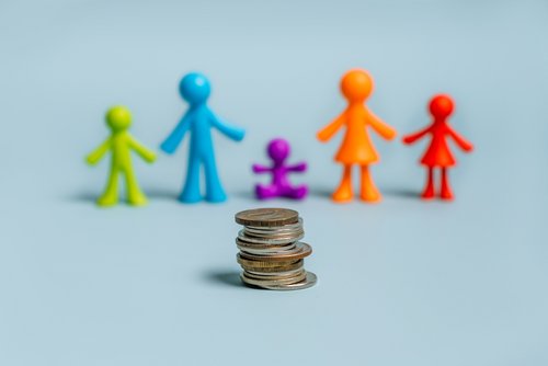 Bunte Figuren von kleinen Männchen, eine Familie auf isoliertem blauem Hintergrund, ein Stapel Münzen im Vordergrund, das Konzept des Familienbudgets und der Sozialleistungen