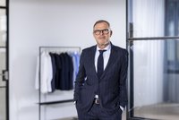 Mark Bezner vor einer Kleiderstange mit Blusen und Hemden