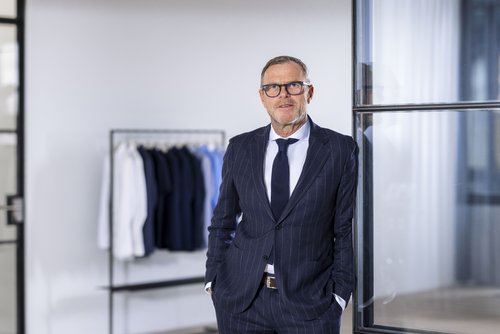 Mark Bezner vor einer Kleiderstange mit Blusen und Hemden