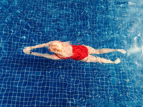Luftaufnahme einer blonden Frau in einem leuchtend roten Einteiler-Badeanzug, die im Becken schwimmt