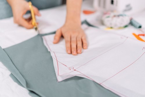 Frau am Schnittmustertisch schneidet Stoff