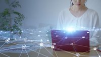 Frau sitzt vor Laptop im Homeoffice. Ein virtuelles Netz schwebt vor ihr