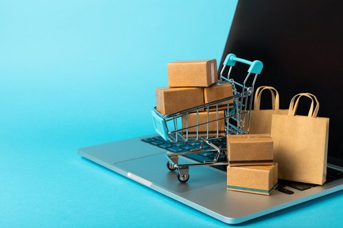Ein Laptop mit mehreren Paketen in einem Einkaufswagen steht auf der Tastatur vor einem blauen Hintergrund.