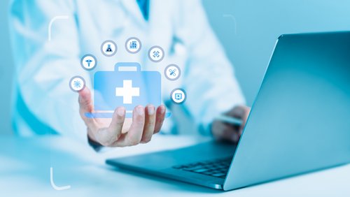 Ein Arzt sitzt vor einem Laptop und hält verschiedene medizinische Symbole digital vor sich.