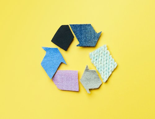Vor einem gelben Hintergrund ordnen sich textile Materialien zu einem Recycling-Kreislauf an.