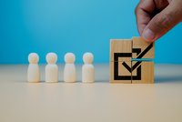 Neben vier weißen Holzfiguren wird ein Quadrat aus Holzwürfeln zusammengesetzt, das eine Zustimmung signalisiert.