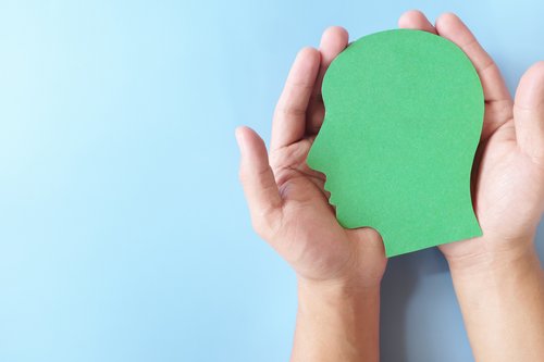 Menschliche Hand, die grüne Kopfprofilsilhouette mit Kopierraum hält. Grüner und nachhaltiger Lebensstil, gesundes Wohlbefinden und psychisches Gesundheitskonzept.