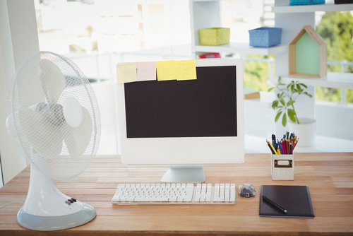 Ventilator auf einem Schreibtisch mit Bildschirm und Haftnotizen