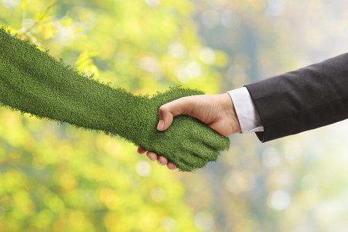 Eine mit Gras bewachsene Hand schüttelt die Hand eines Menschen mit Anzug.