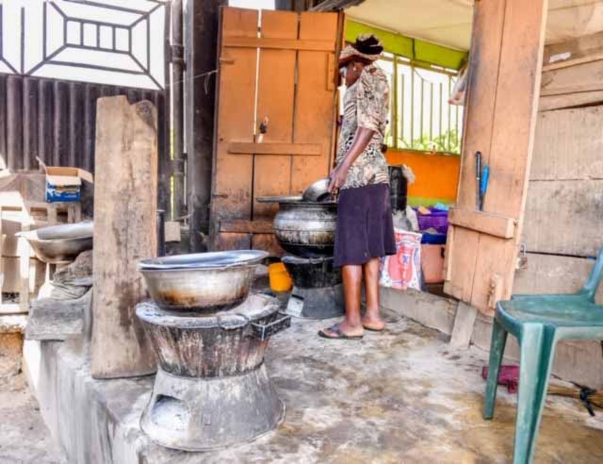 Vor einer Haustür stehen mehrere Kochöfen, vor einem steht eine nigerianische Frau.