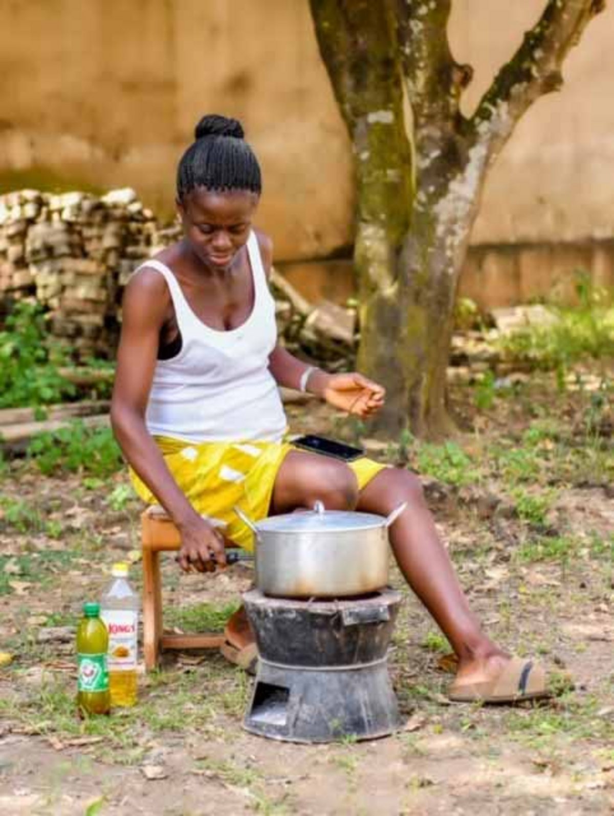 Eine Frau in einem weißen Top und gelbem Rock sitzt vor einem Kochofen in Nigeria.
