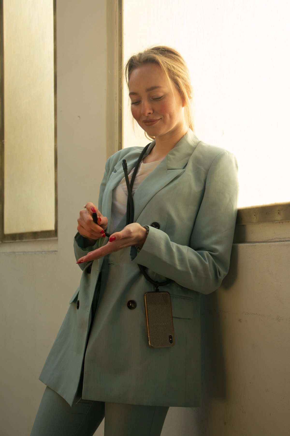 Junge Frau in hellblaume Blazer lehnt im Fenster und sprüht Desinfektionsspray aus Handykette von PortHy in die Hand.