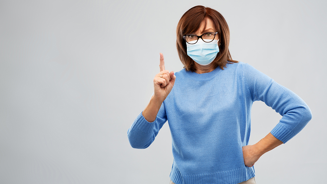 Frau in blauem Pullover und Maske hebt mahnend den Zeigefinger