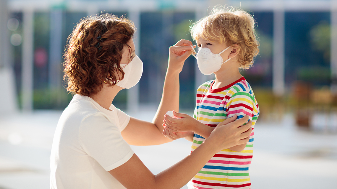 Frau mit Maske richtet kleinem Kind Maske