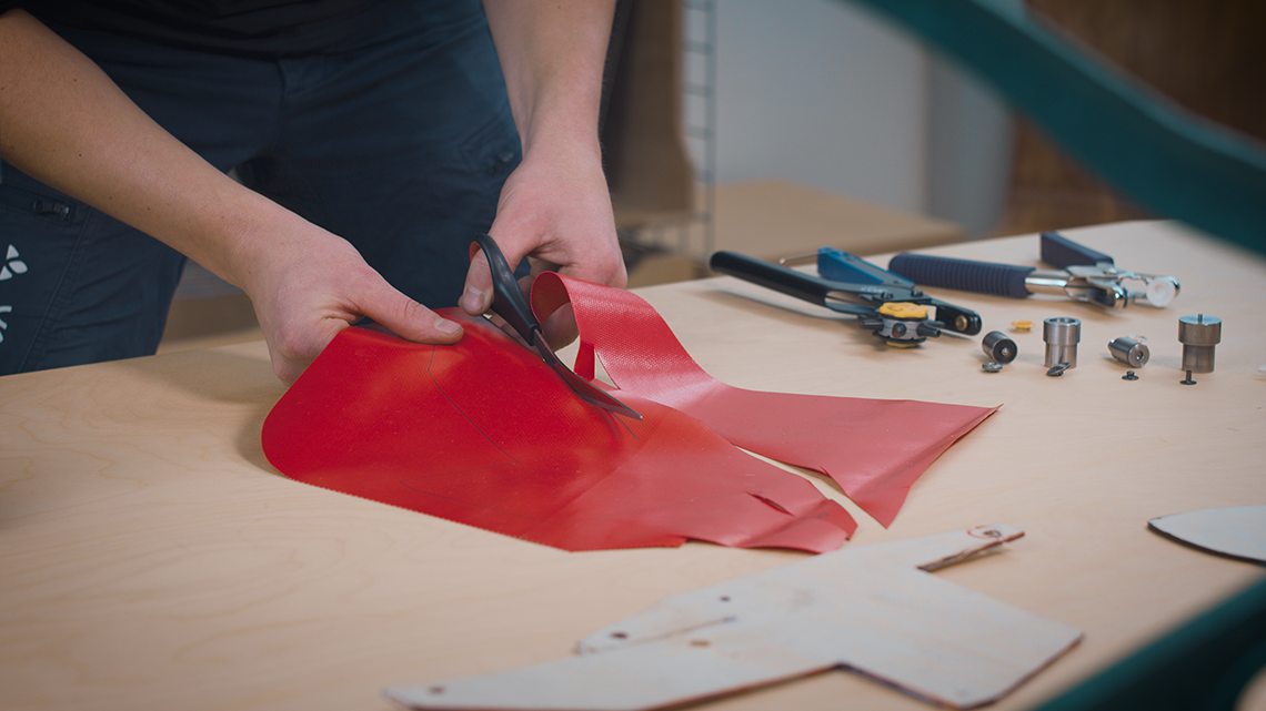 Hand schneidet rotes Material mit Schere klein. Anderes Werkzeug liegt im Hintergrund