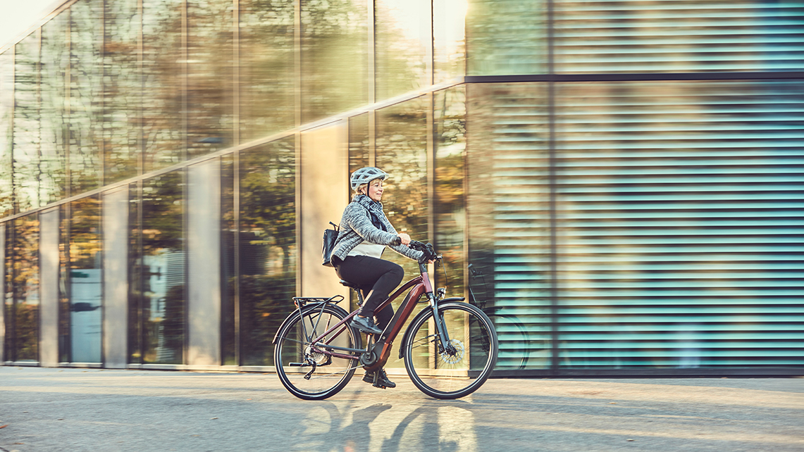 Frau mit Helm fährt mit einem E-Bike an einem Bürogebäude entlang.