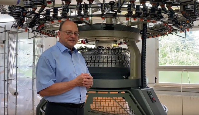 Der Geschäftsführer der roma Strickstoff-Fabrik Rolf Mayer GmbH & Co. KG steht vor einer Strickmaschine.