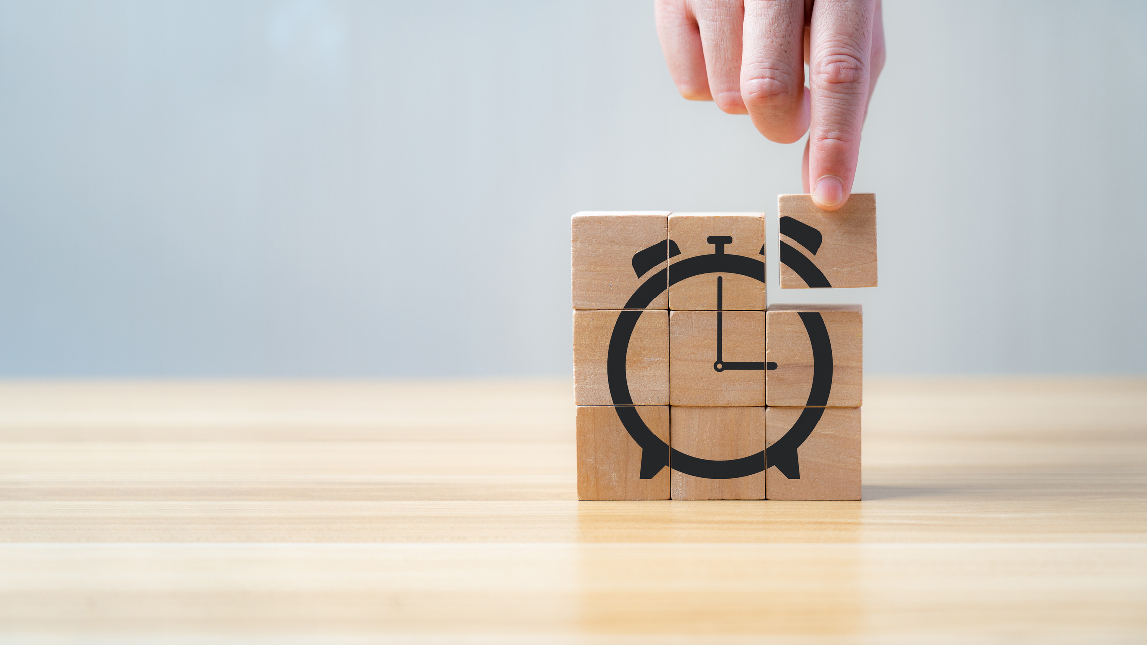 Eine Hand ergänzt ein Stück Holzmosaik, sodass das fertige Puzzle eine Uhr ergibt.