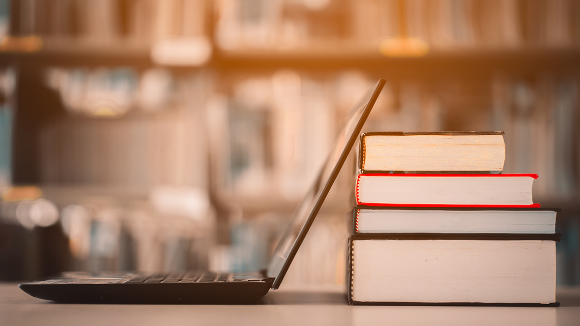 Aufgeklappter Laptop lehnt an einem Stapel Bücher