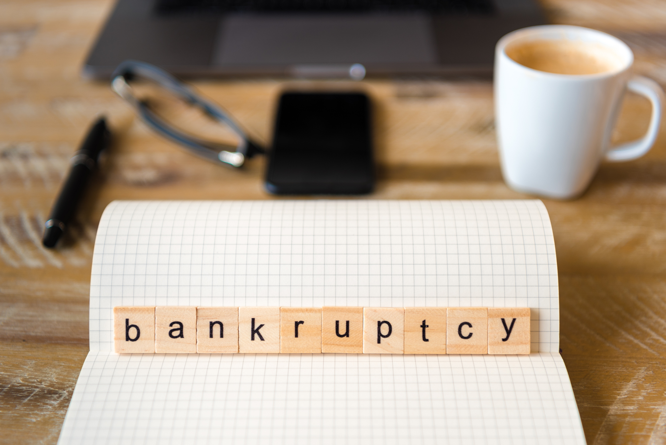 Auf einem Schreibtisch liegen auf einem Papierblock verschiedene Buchstaben, die das Wort "Bankruptcy" (Insolvenz) bilden.