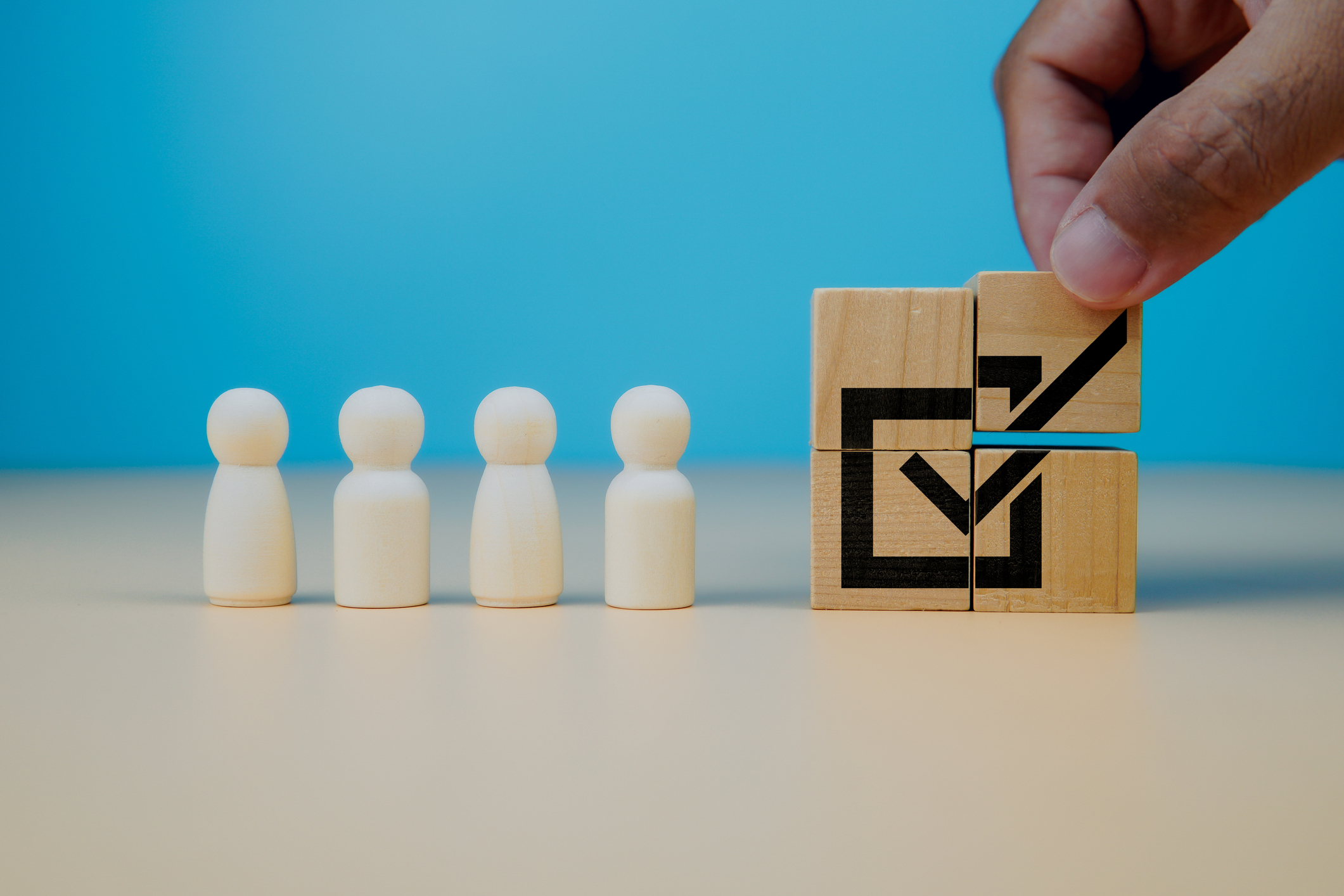 Neben vier weißen Holzfiguren wird ein Quadrat aus Holzwürfeln zusammengesetzt, das eine Zustimmung signalisiert.