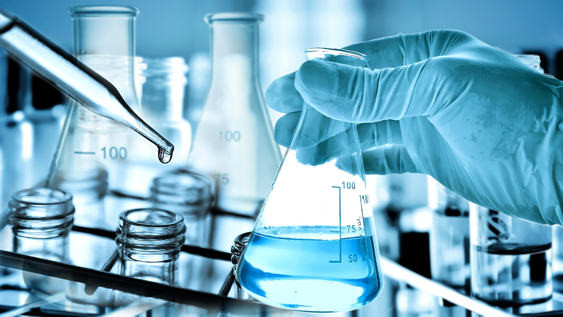 Behandschuhte Hand hält ein mit bläulicher Flüssigkeit gefülltes Reagenzglas dem sich eine Pipette nähert.