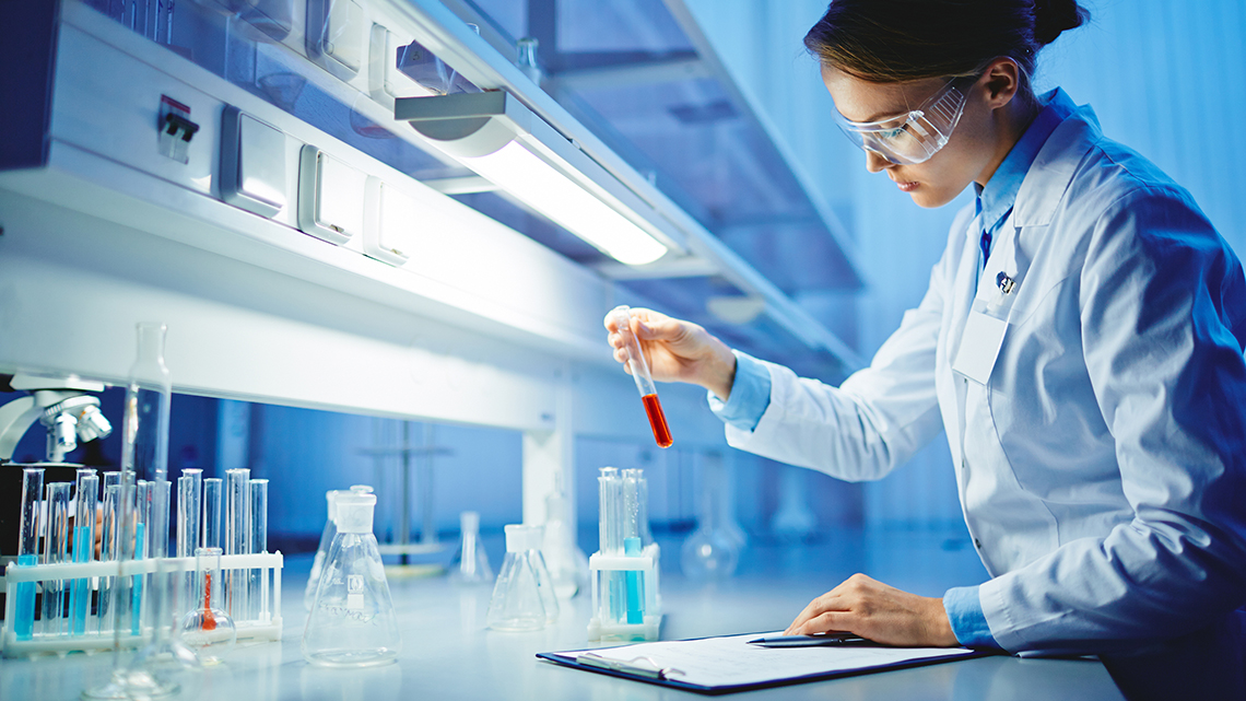 In einem Chemikalienlabor überprüft eine Frau mit Schutzkleidung und Brille mehrere Proben.