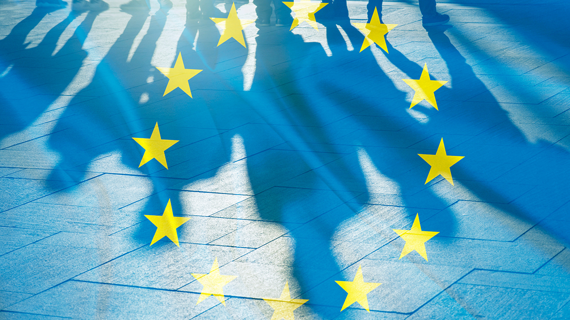Vor der verblassten europäische Fahne sind die Schatten einiger Menschen zu sehen.