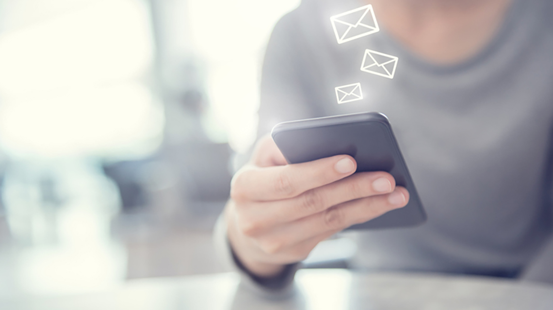 Person in grauem Oberteil sitzt vor Telefon aus dem virtuelle Briefumschläge aufsteigen.