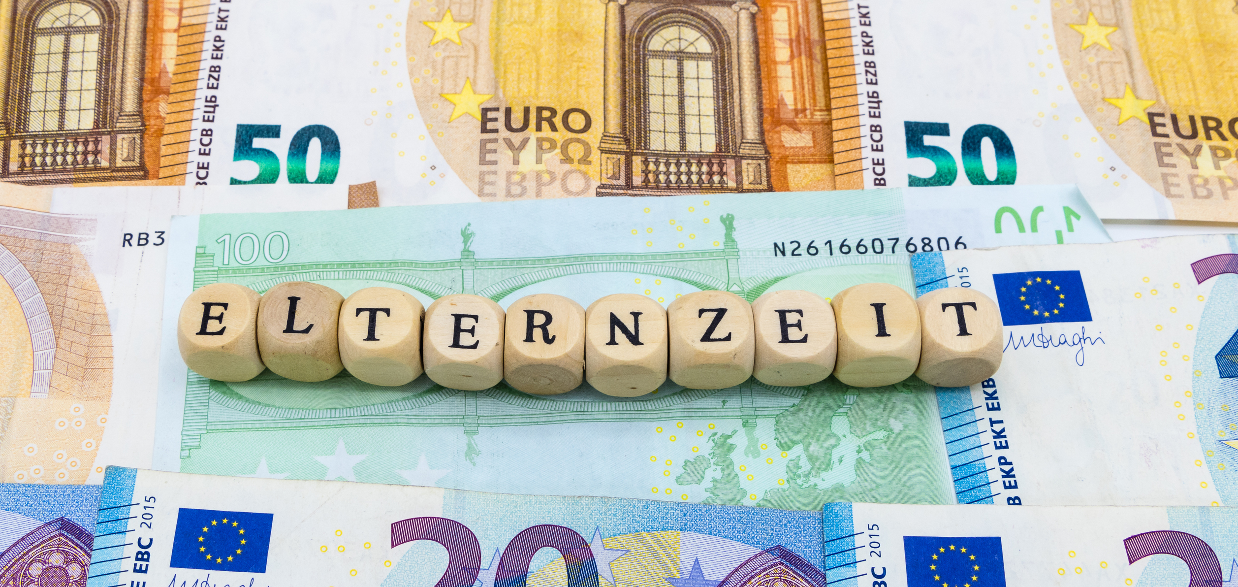 Holzwürfel mit Text "Elternzeit" liegen auf Euroscheinen