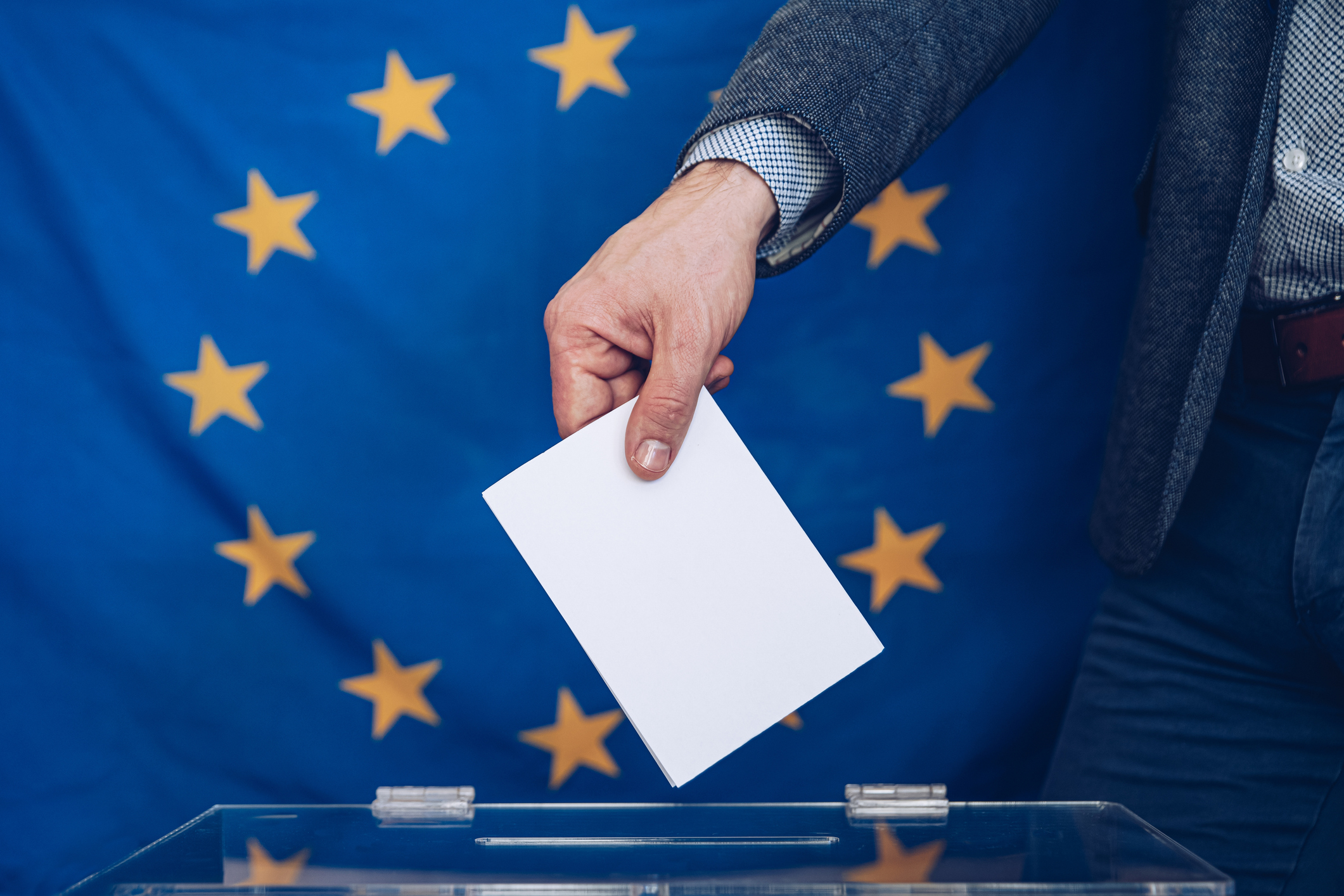 Eine Hand wirft einen Umschlag in eine Wahlurne vor der Europafahne.