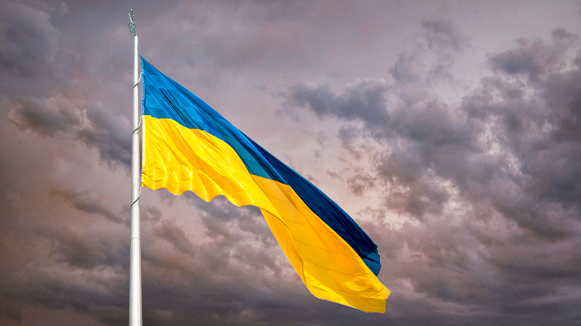 Vor einem dunklen Himmel weht die Ukraine Fahne. 