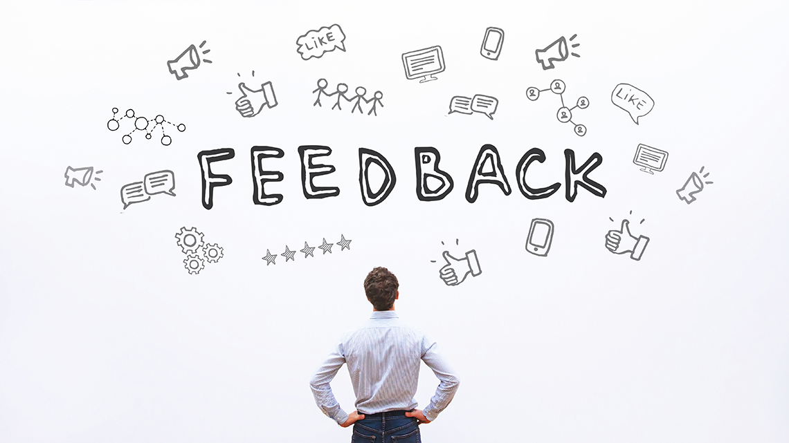 Ein Mann im Hemd steht vor einer Wand mit der Aufschrift Feedback und vielen Symbolen.