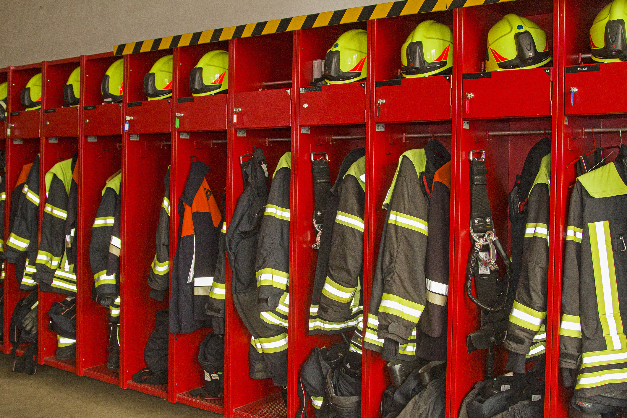 Auf einer Feuerwache sind rote Spinde gefüllt mit Helmen und Anzügen zu sehen. Alles ist bereit für den nächsten Einsatz.