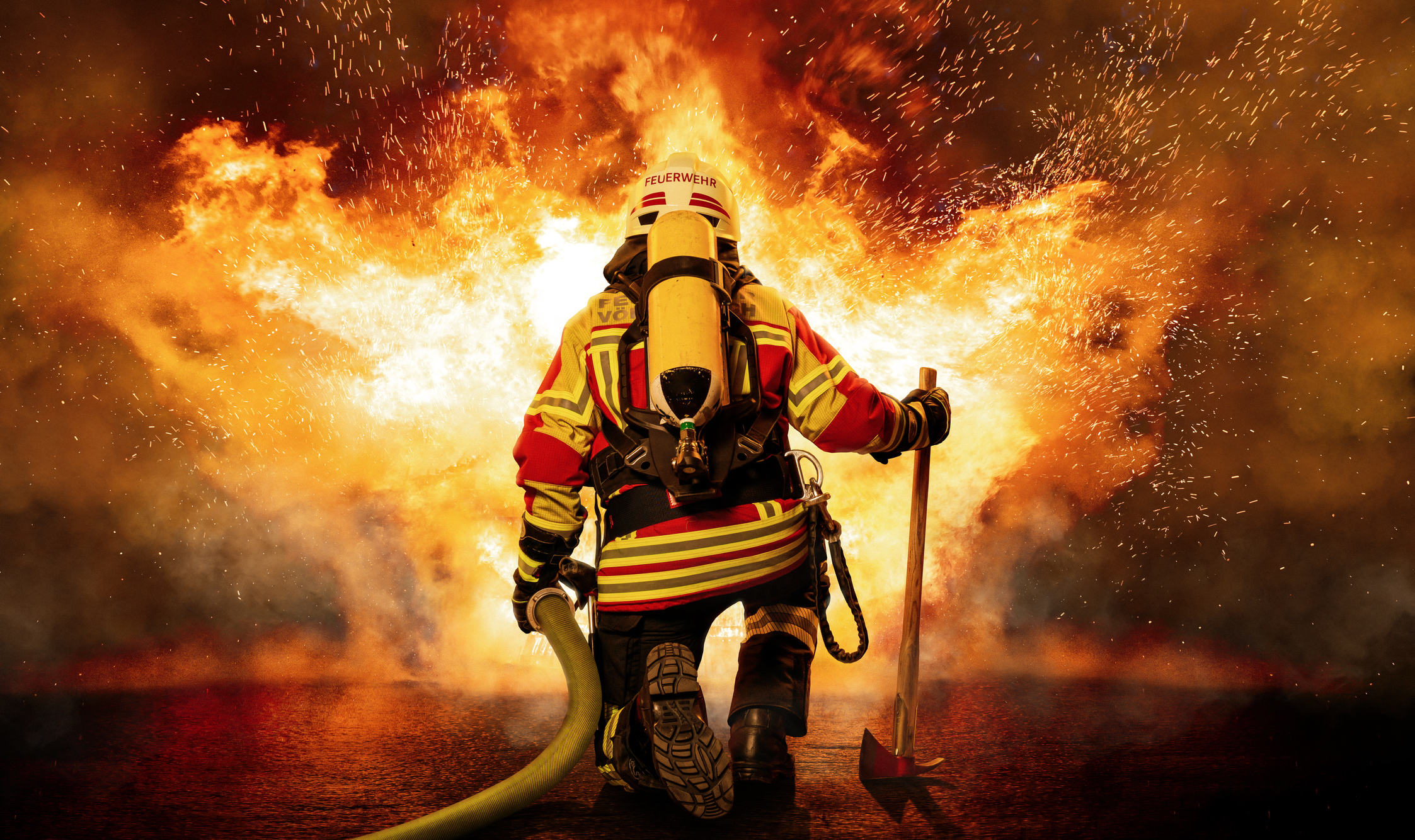 Feuerwehrmann in voller Montur kniet vor einem Feuer