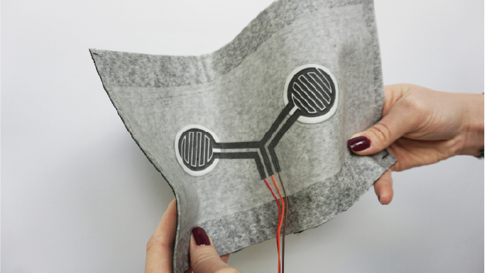 Der hellgraue textile Sensor eines Smart Seats wird in den Händen gehalten und leicht gebogen.