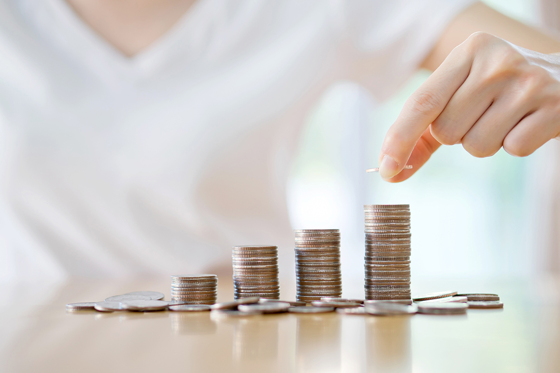 Hand zählt Geld auf mehreren Münzstapeln