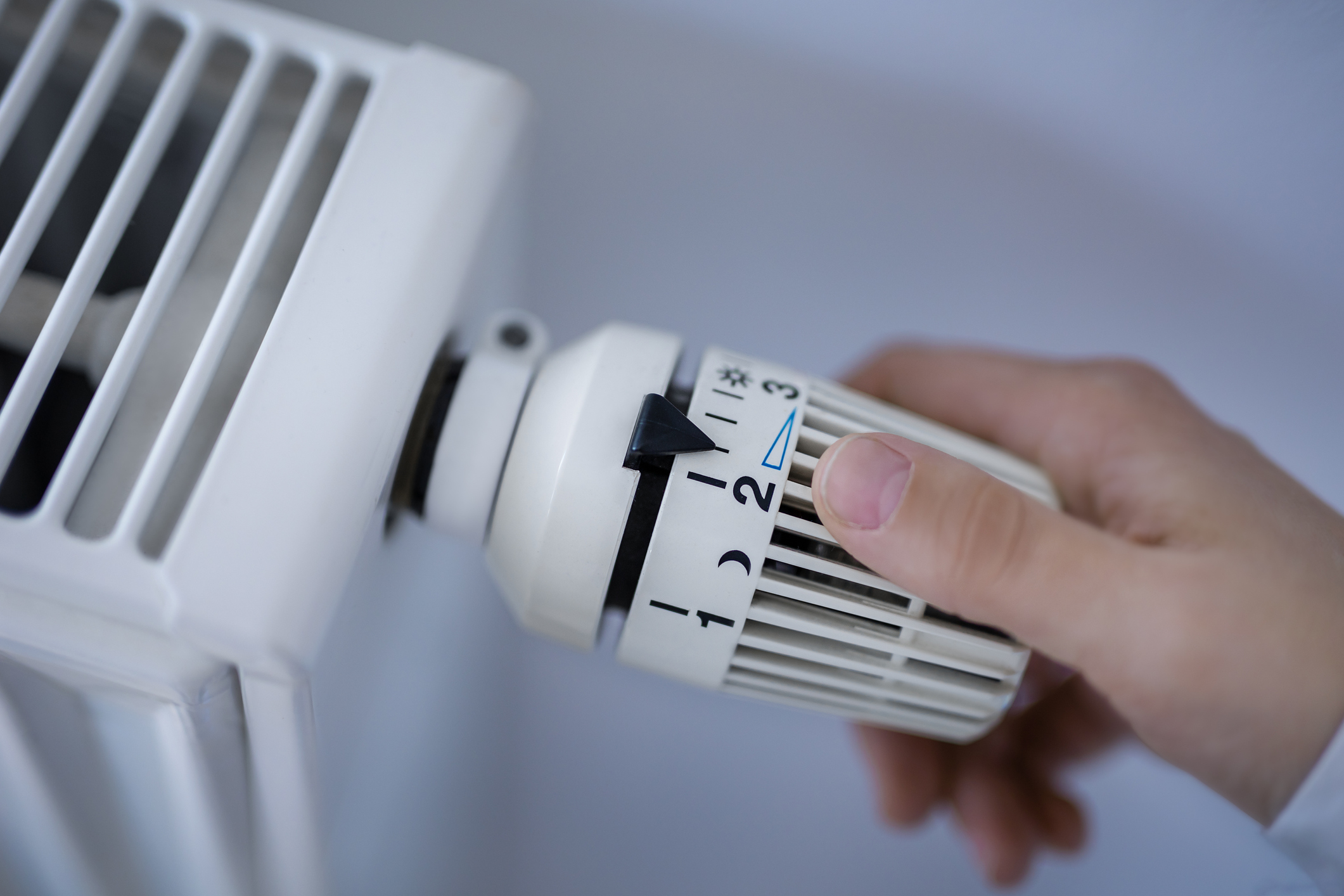 Eine Hand dreht an dem Thermostat einer Heizung und stellt diese kälter.