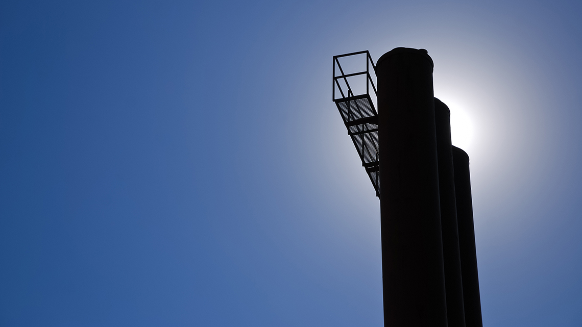 Der Schornstein einer Industrieanlage zeichnet sich vor einem strahlend blauen Himmel ab.