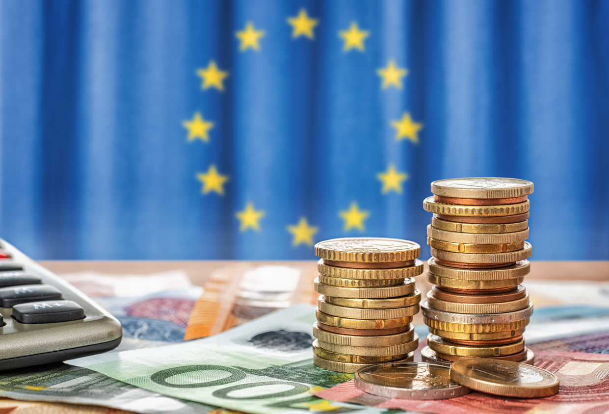 Münzen und Euroscheine vor EU-Flagge auf dem Tisch