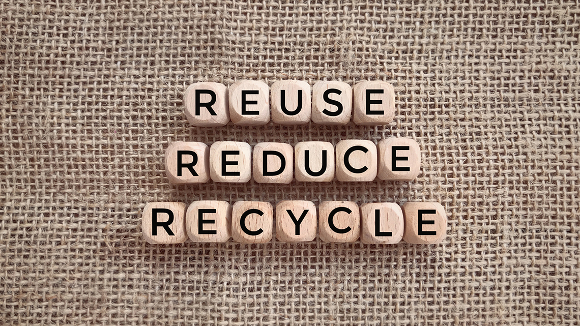 Auf einem Jutebeutel liegen Buchstabenwürfel, die die Wörter Reuse, Reduce und Reycle bilden. 