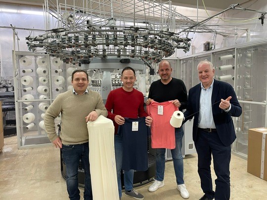Die vier Repräsentanten der drei Lokalstoffmacher vor einer Textilmaschine.