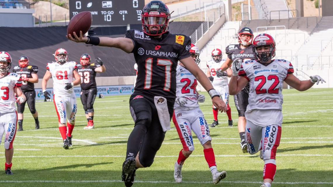 Während eines Footballspiels springt ein Spieler in schwarzem Trikot und holt zum Wurf aus. 